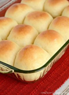 a casserole dish filled with rolls on top of a red place mat next to a glass container