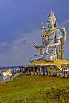 a large white statue sitting on top of a lush green field next to the ocean