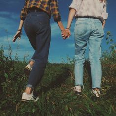 two people holding hands walking through the grass