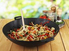 a pan filled with pasta and vegetables on top of a wooden table next to spices