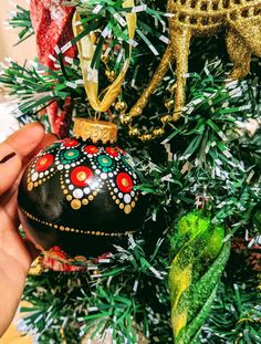 a hand holding an ornament in front of a christmas tree with ornaments on it