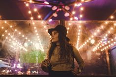 a woman wearing a hat standing in front of a stage with lights on the wall