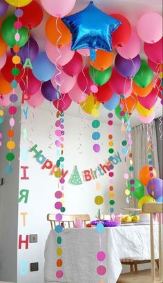 balloons and streamers are hanging from the ceiling in this birthday party room with white table cloths