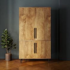 a wooden cabinet sitting on top of a hard wood floor next to a potted plant