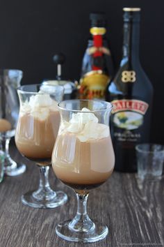 two glasses filled with ice cream sitting on top of a wooden table next to bottles