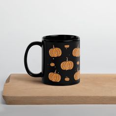 a black mug with orange pumpkins on it sitting on top of a wooden table