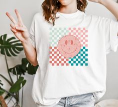 D E S I G N Super trendy checkered happy face tee!  This classic unisex jersey short sleeve tee fits like a well-loved favorite. Soft cotton and quality print make buyers fall in love with it over and over again. You can roll the sleeves or tie it in a knot for a super trendy look. The soft-washed, garment-dyed fabric brings extra coziness to your wardrobe while the relaxed fit makes it an excellent daily choice. Comfort Colors Unisex Garment-Dyed T-shirt S I Z I N G Please refer to the SIZE CHART in the listing photos to ensure you get the perfect fit. S M L XL XXL XXXL D E T A I L S Brand - Comfort Colors Relaxed fit Midweight Tee Pre-shrunk fabric Solid Colors: 100% combed and ring-spun cotton -direct-to-garment or DTG printing used for most of our apparel products -DTG printing yields Younglife Shirt, Checkered Shirt Outfit, Checkered Shirt, Graphic Tee Shirt, Dtg Printing, Retro Shirts, T Shirt Oversized, Happy Face, Dyed Fabric