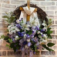 a cross hanging on a brick wall next to a wreath with purple and white flowers