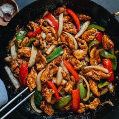 chicken stir fry with peppers and onions in a wok on a table next to chopsticks