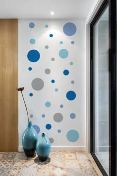 two blue vases sitting in front of a wall with polka dot decals on it