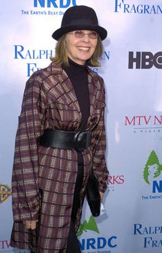 a woman in plaid coat and black hat standing on the red carpet at an event