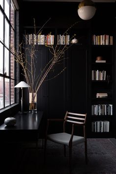 a black room with bookshelves and a chair next to a table in front of a window