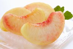 two slices of peaches sitting on top of ice with mint sprigs in the background