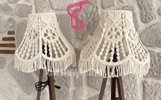 two white lamps with tassels on them sitting next to each other in front of a stone wall