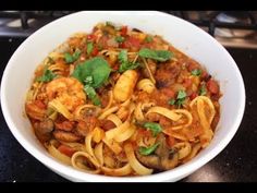 a white bowl filled with pasta and shrimp on top of a black counter next to a stove