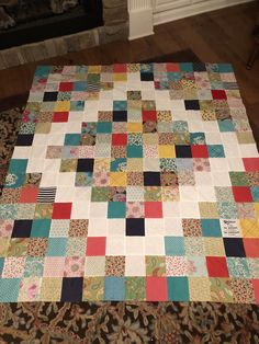 a multicolored patchwork quilt is laying on the floor next to a fireplace