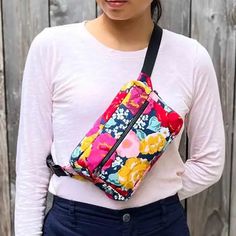 a woman wearing a white shirt and black pants holding a colorful floral bag in front of a wooden fence