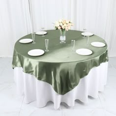 a green table cloth with white plates and vases on the top is set for a formal dinner