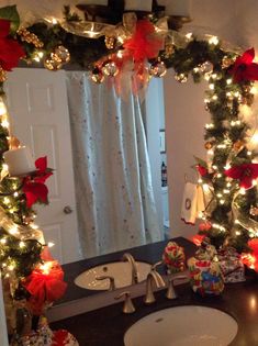 a bathroom decorated for christmas with lights on the mirror and wreaths around the sink