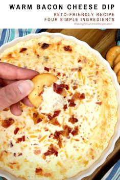 a hand holding a cracker over a cheesy dip in a white bowl