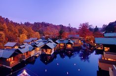 an aerial view of several resort buildings at dusk with lights on the water and trees in the background