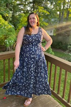 a woman is standing on a deck wearing a blue dress and smiling at the camera