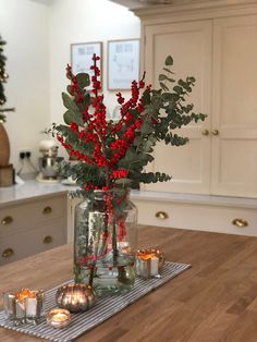 a vase filled with red berries and greenery sitting on top of a wooden table