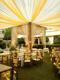 an outdoor wedding venue with yellow and white draping on the ceiling, decorated with gold ribbon