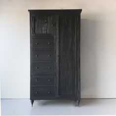 an old black armoire with drawers and knobs on the doors is against a white wall