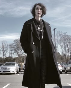 a woman standing in the middle of a parking lot wearing a black coat and cross necklace