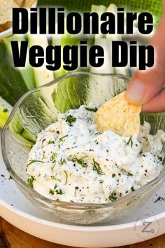 someone dipping dip into a glass bowl with vegetables in the background and text overlay reading difflonaire veggie dip