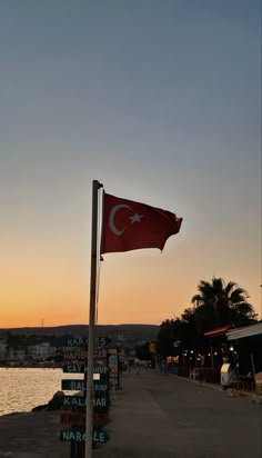 a red flag on the side of a road next to water and buildings at sunset