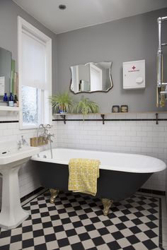 a black and white checkered floor bathroom with a claw foot bathtub, pedestal sink, and mirror