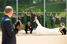 a woman in a wedding dress standing next to a man on a baseball field with people behind her