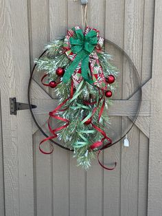 a christmas wreath hanging on the side of a wooden door with red and green ribbons