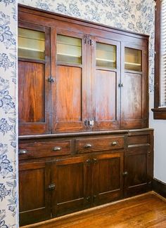 an old wooden cabinet with glass doors in a room that has blue and white wallpaper on the walls