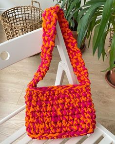 an orange and pink purse sitting on top of a white chair next to a potted plant