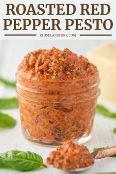 a jar filled with roasted red pepper paste on top of a white table next to basil leaves