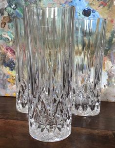 two clear glass vases sitting on top of a wooden table next to a painting