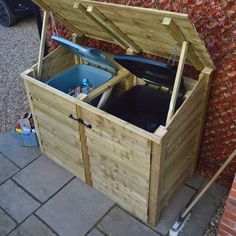 an outdoor storage box with the lid open and two trash cans in it next to a brick wall