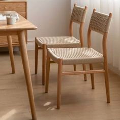 two wooden chairs sitting next to each other near a table with a cup on it