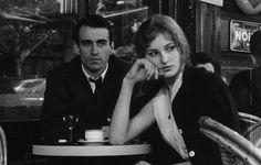 black and white photograph of two people sitting at a table in a restaurant, one man is holding his hand to his ear