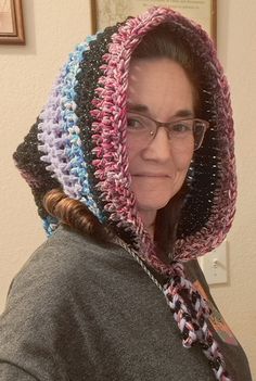 a woman with glasses wearing a crocheted hood over her head and scarf around her neck