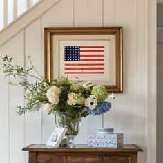 a vase filled with flowers sitting on top of a wooden table next to a framed american flag