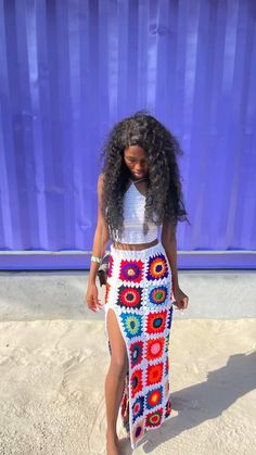 a woman standing in front of a blue wall wearing a colorful crochet skirt