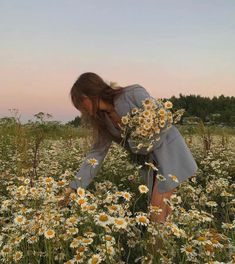 a woman kneeling down in a field of daisies