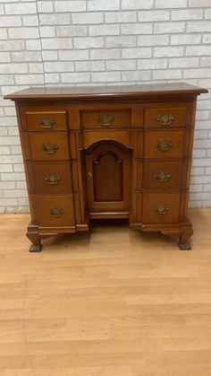 an old wooden desk with two drawers and one door on the top, in front of a brick wall