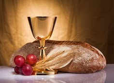 bread, grapes and a chalice on a table with a light in the background