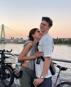 a man and woman standing next to each other on a bridge with bicycles in the background