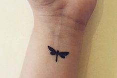 a small black dragonfly tattoo on the wrist